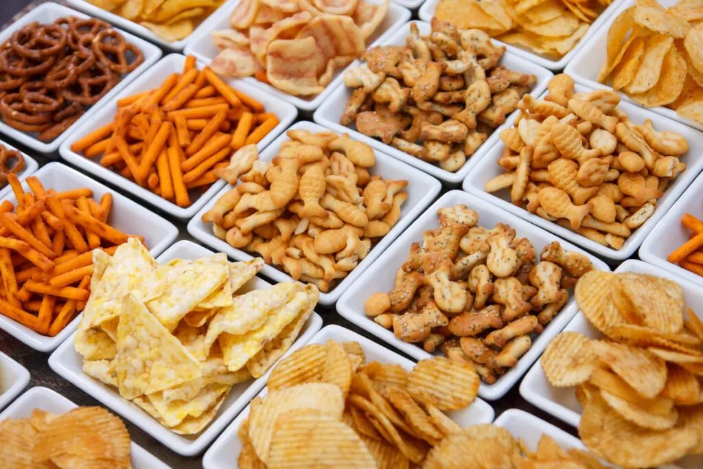 Assorted snack foods including pretzels, crackers, and chips in white bowls